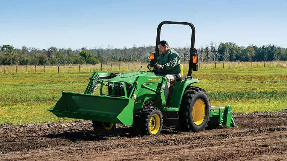 Man driving compact utility tractor over dirt field