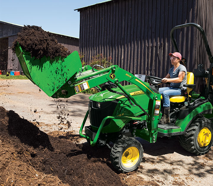 John Deere 1025R sub-compact tractor loading the bucket with dirt.