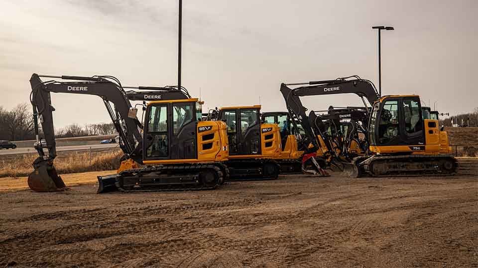 Compact excavators lined up on dealership lot Compact excavators in line on dealership lot