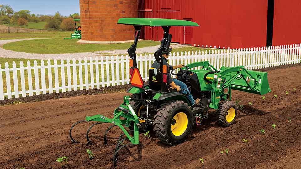 Compact utility tractor pulling rake through dirt field