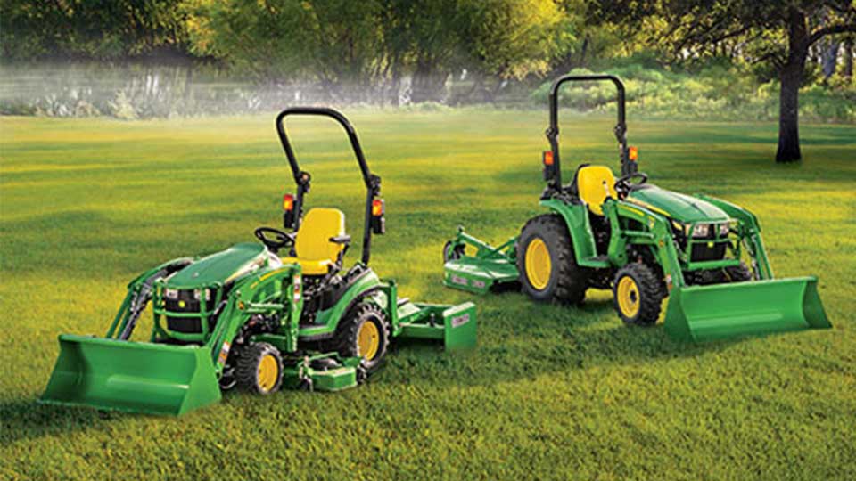 two John Deere subcompact tractors in grass field