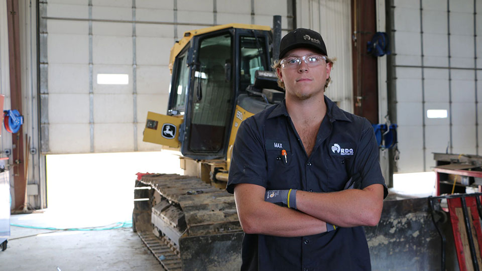 technician arms crossed looking at carmera in front of bulldozer