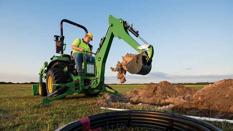 John Deere compact utility tractor with loader digging hole