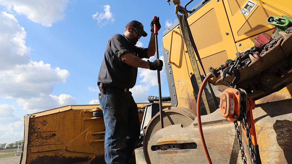 service technician working on backhoe on construction site