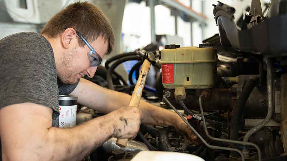 service technician working on engine with hammer