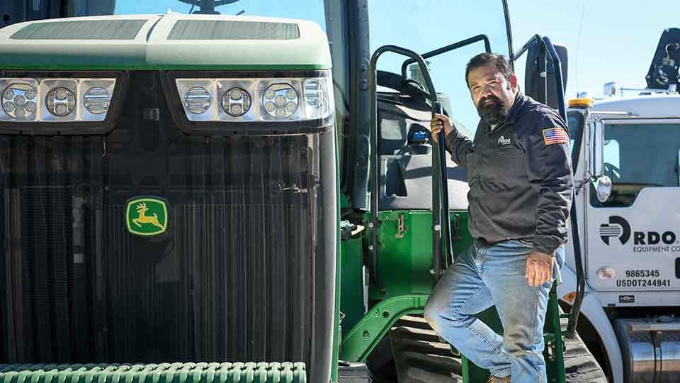 Diesel mechanic standing on ladder John Deere tractor