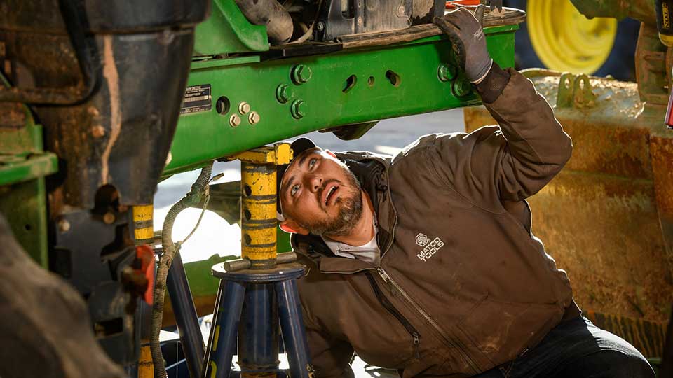 diesel mechanic looking at underside of tractor