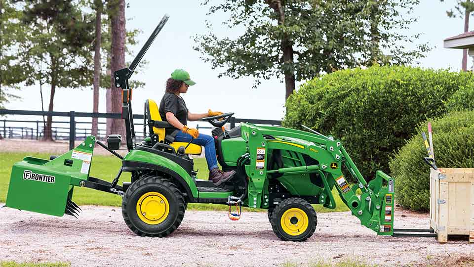 Woman using pallet forks on sub compact tractor
